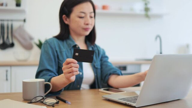 Homebody behind laptop looking at bank card in kitchen