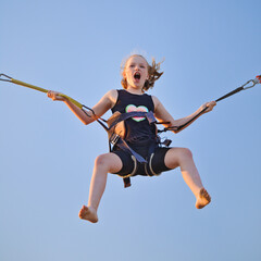 Little white girl child jumping on a trampoline with insurance elastic bands in an amusement park and carousels.