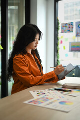 Pretty Asian female graphic designer drawing something on digital tablet working on new design project at creative office