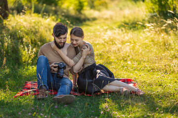 young couple sits in nature and looks at the camera at the resulting picture