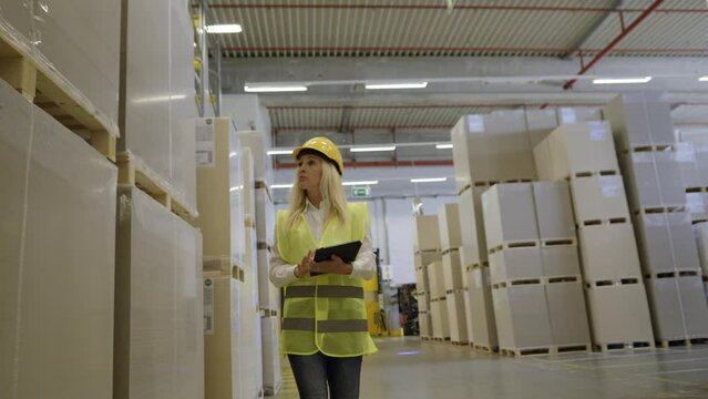 Industrial warehouse woman employee using digital tablet and walking front view handheld tracking shot. Distribution manager checking merchandise in storehouse