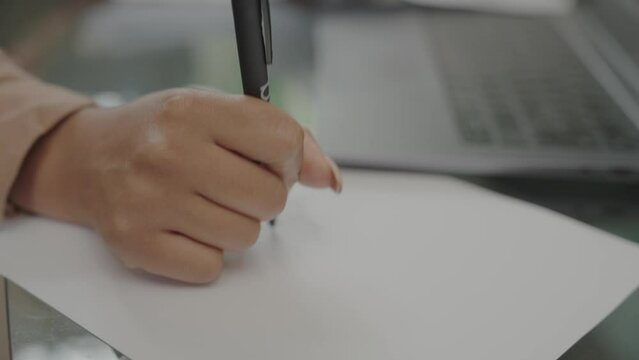 Woman's hand writing on paper at desk