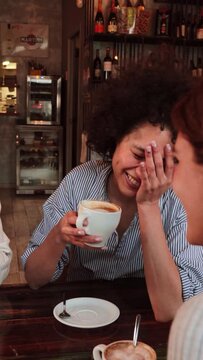 Vertical portrait of a young women talking and laughing sitting on a coffee shop or restaurant. Two ladies smiling and looking his friend holding a cup. Girls having fun chatting on a bar. High