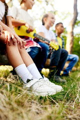 Happy kids sitting on log in forest on sunny day, playing guitar, having fun. Going hiking, walking, active weekends. Concept of leisure activity, childhood, summer, friendship, active lifestyle