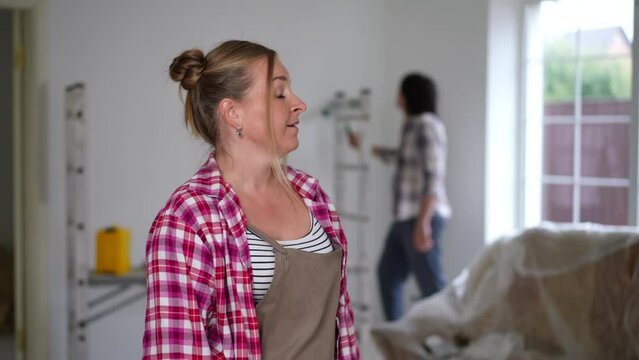 Plus-size woman looking back at man painting wall in slow motion turning rolling eyes sighing. Portrait of dissatisfied Caucasian lady on the left in new house under repair