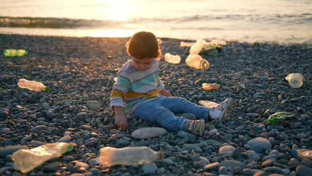 a small child is sitting playing among plastic garbage on the beach