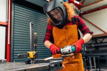 Fototapeta premium A self-taught girl grinds in the workshop, uses a visor and gloves for protection