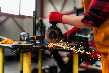 Close-up of a woman in STEM using grinder to cut a metal bar, wearing gloves and a apron sparks...