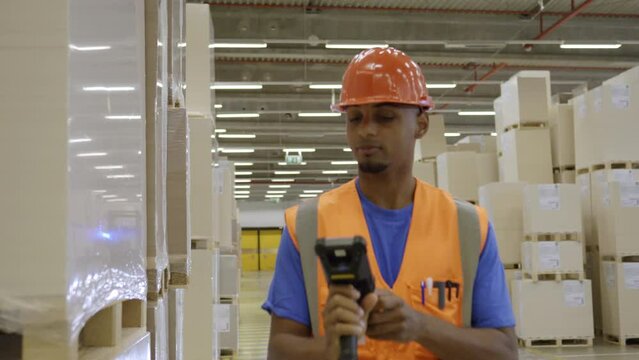 Warehouse worker scanning goods barcode, smiling and looking at camera. African american man using bar code scanner in industrial storehouse portrait