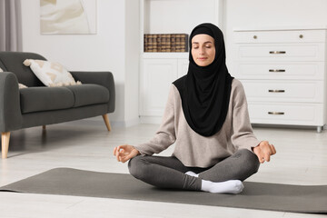 Muslim woman in hijab meditating on fitness mat at home. Space for text