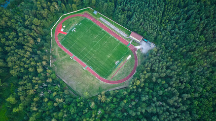 Drone top down view of town football field in summer deciduous forest. Calm cloudy day from tall green trees around. Football field, aerial shot.