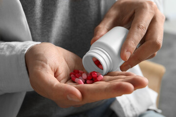 Man pouring pills from bottle on blurred background, closeup