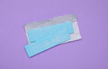 Sticks of tasty chewing gum on violet background, flat lay