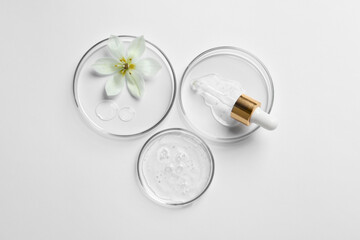Petri dishes with samples of cosmetic oil, pipette and beautiful flower on white background, flat...
