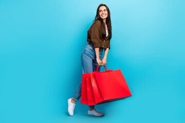Full body length cadre of dreamy young fashionista woman holding red packages bargains sale purchase ad isolated on blue color background