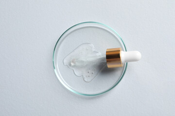 Petri dish with sample of cosmetic oil and pipette on white background, top view