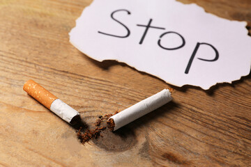 Broken cigarette and word Stop written on paper on wooden table, closeup. No smoking concept