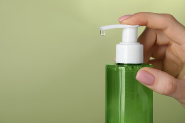 Woman using cleansing gel on pale olive background, closeup. Space for text
