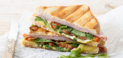 Panini sandwich with ham, cheese, tomato and arugula on wooden table. Panorama view