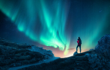 Northern lights and young woman on mountain peak at night. Auror - obrazy, fototapety, plakaty