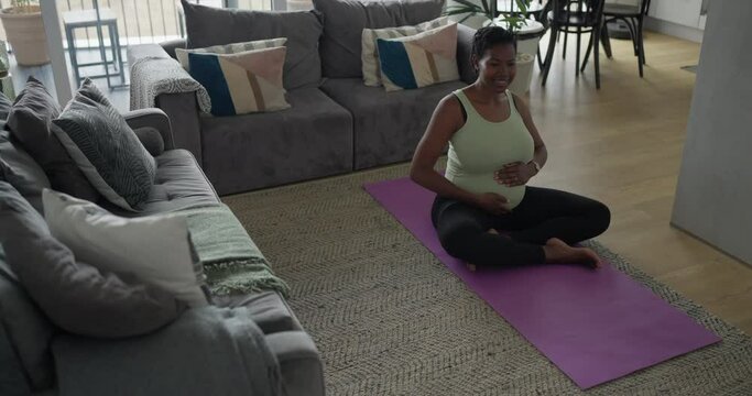 Pregnant woman touching belly on exercise mat in living room