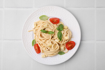 Delicious pasta with brie cheese, tomatoes and basil leaves on white tiled table, top view
