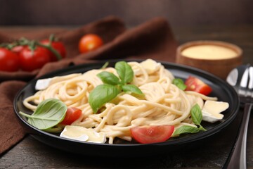 Delicious pasta with brie cheese, tomatoes and basil leaves on table, closeup