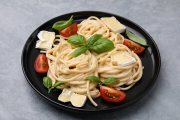 Delicious pasta with brie cheese, tomatoes and basil leaves on grey table, closeup
