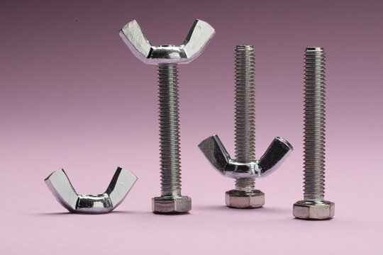 Three metal screws with wing nuts on purple background