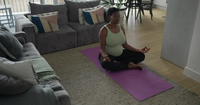 Pregnant woman sitting in lotus position on exercise mat in living room