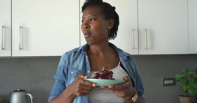 Portrait of pregnant woman eating red grapes in kitchen