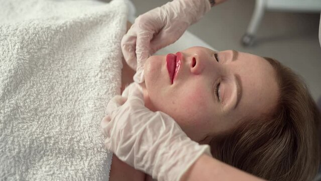 Professional cosmetic procedures. Young female doctor in a beauty clinic receiving facial microdermabrasion treatment. After the procedure, the master cosmetologist wipes the face from the cream.