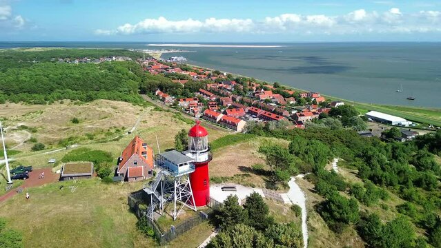 Aerial drone image of Vlieland. With bright red Lighthouse on top of a dune overlooking the small town, the North Sea and the Wadden Sea on a bright summer day. High quality stock film