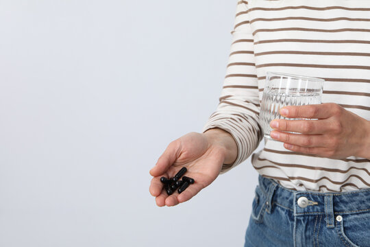 A woman is holding tablets of activated charcoal on a light background