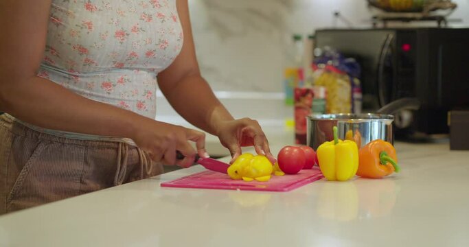 Woman cutting yellow bell pepper in kitchen