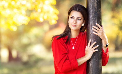 Young woman leans on tree and looks