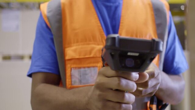Warehouse worker holding barcode scanner and using management system close up. Storehouse employee in safety vest holding handheld bar code reader device closeup
