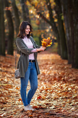 Young woman is standing in the forest with a rush of colorful leaves