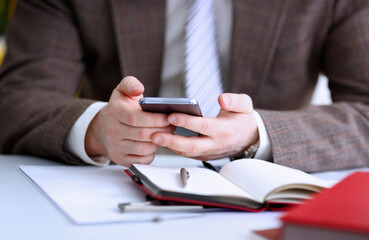 Male arm in suit hold phone and silver pen at workplace closeup. Read news mania send sms chat...
