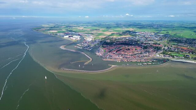 Aerial drone footage, film, of the seaport of Harlingen in Friesland, The Netherlands. Different color of water due to currents in the Wadden Sea. Pier, jetty and old town visible. Green meadows.