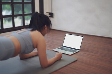 A young Asian woman with practicing Yoga and exercise online with a trainer learning laptop on a yoga mat at home.
