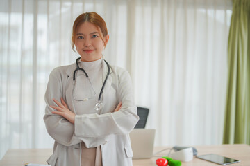Asian doctor woman standing smiling with crossed arms and stethoscopein the medical office.