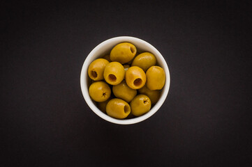 Green olives in a white bowl on a black background