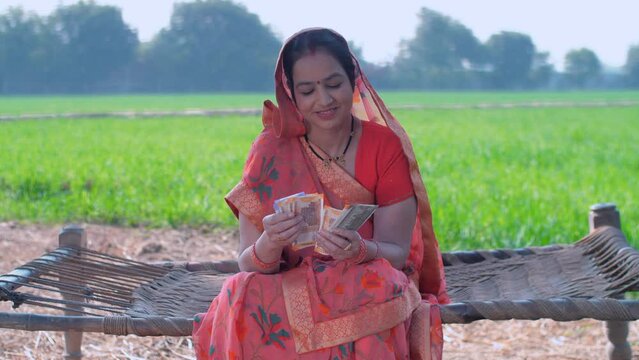 A mid-aged female farmer counting her hard-earned money - monthly income  agricultural loan  breadwinner of family. Village woman counting money - government grant money  agriculture scheme money  ...