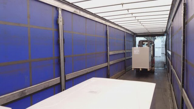 Warehouse forklift driver loading boxes in cargo shipping container, view from inside of storage. Storehouse employee on lift truck lifting merchandise, preparing freight for transportation