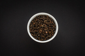 Dried black pepper seeds in a white bowl on black background