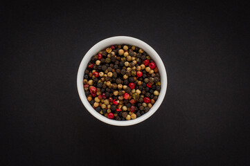 Mixed dried pepper seeds in a white bowl on black background