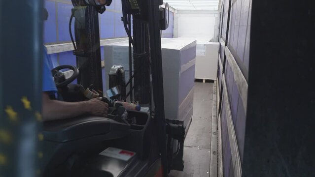 Warehouse forklift loading boxes in shipment truck, view from inside trunk container. Storehouse loader putting parcels in trailer vehicle for transportation