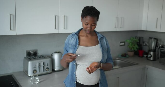 Pregnant woman taking supplements in kitchen