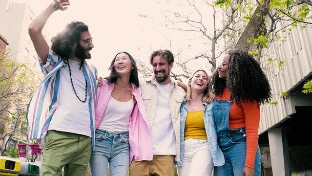 Diverse group of cheerful millennial friends standing together hugging each other in street. Cheerful multiethnic young carefree friends laughing and having fun looking at camera.